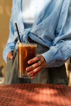 Close-up of a stylish Woman standing by an outdoor cafe table holding an iced espresso tonic drink