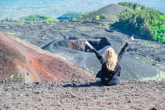 Rear view of a carefree Woman sitting on Mt Etna with her arms in the air, Sicily, Italy