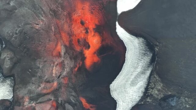 Aerial view of Maelifellssandur volcanic landscape with vibrant red mineral deposits contrasting against black lava fields and white snow in Kirkjubaejarklaustur, Skaftarhreppur, Iceland.