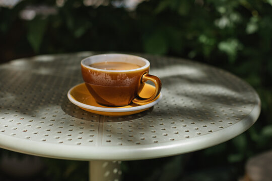 Close-up of a cup of white coffee on an outdoor cafe table on a summer day
