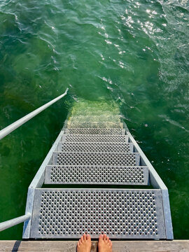 Overhead view of a barefoot woman standing on a pier by metal steps into the sea on a summer day, Samsoe, Jutland, Denmark
