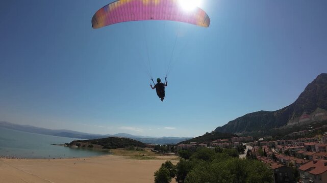 Aerial view of a paraglider soaring above the beach and urban landscape of Egirdir Lake in Egirdir, Isparta, Turkiye.