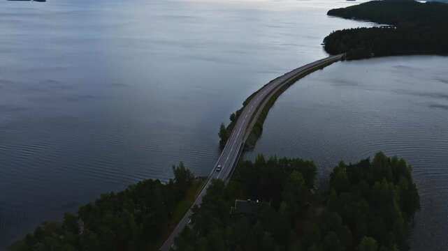 Aerial view of the Pulkkilanharju ridge road crossing the lake surrounded by dense forests in Asikkala, Paijat-Hame, Finland.