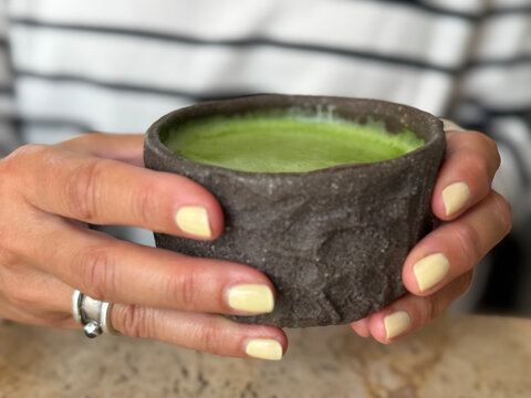 Close-up of a woman sitting at a table holding a traditional earthenware cup with a premium matcha tea drink