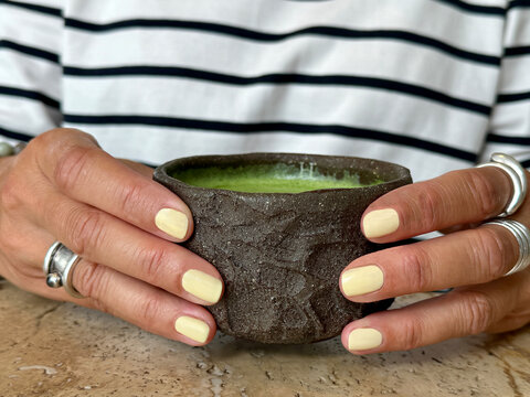 Close-up of a woman sitting at a table holding a traditional earthenware cup with a premium matcha tea drink