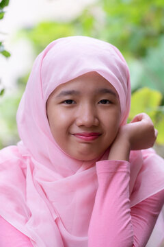 Close-up Portrait of a smiling Teenage Girl in a Pink Hijab sitting outdoors