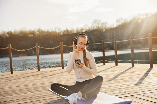 Portrait of female model relaxing after yoga workout. Pretty woman listening to music with headphones outdoors. Wellness concept.