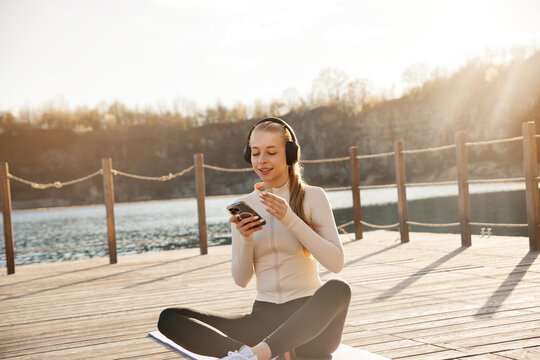 Young woman listening to music after fitness training. Beauty woman using smartphone while relaxing on yoga mat. Active lifestyle concept.