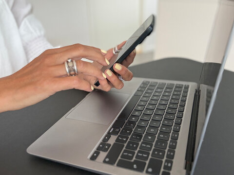 Close-up side view of a businesswoman sitting at desk with her laptop computer and using a mobile phone
