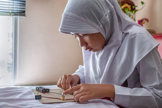 Close-up side view of a teenage girl in a hijab sitting at a table making an electronic Circuit