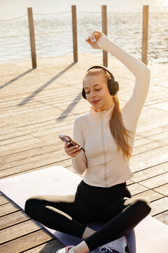 Portrait of female model smiling with smartphone outdoors. Beautiful woman enjoying headphones after yoga practice. Active lifestyle concept.