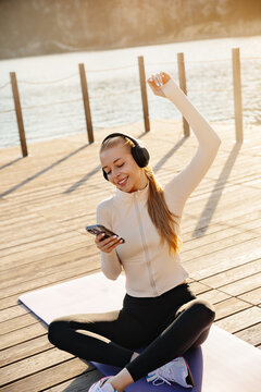 Beauty woman smiling while reading smartphone outdoors. Pretty woman relaxing with headphones after fitness workout. Healthy living concept.