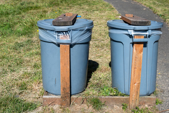 DIY, do it yourself, animal and wind proofed garbage cans, plastic trash bins reinforced with wood boards outdoors in a public park
