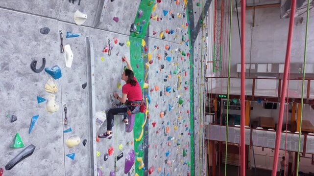 Indoor sport climber ascending steep artificial climbing walls on colorful routes while secured with ropes and harnesses, demonstrating balance, strength, technique and concentration during training.