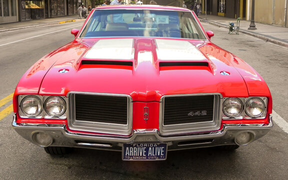 A symmetrical front-view shot of a classic 1971 Oldsmobile 442 muscle car in bright red with white hood stripes. 