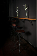 interior of a pub, wooden bar stools at counter in dark moody pub interior with white Dianthus caryophyllus flowers in small vases close up, hospitality venue stock photography with copy space © liligluck