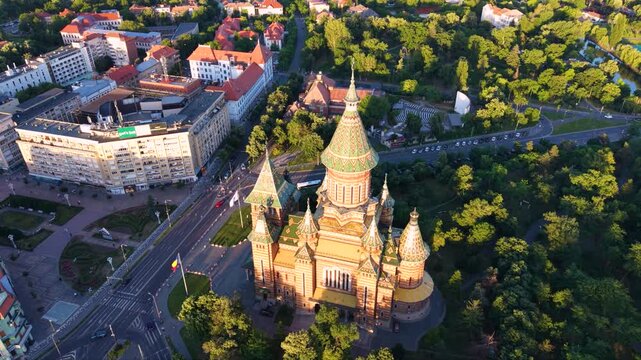 Aerial view of the Romanian Orthodox Metropolitan Cathedral in Timișoara, Romania, surrounded by dense green parkland, city streets and historic buildings in warm golden-hour light.