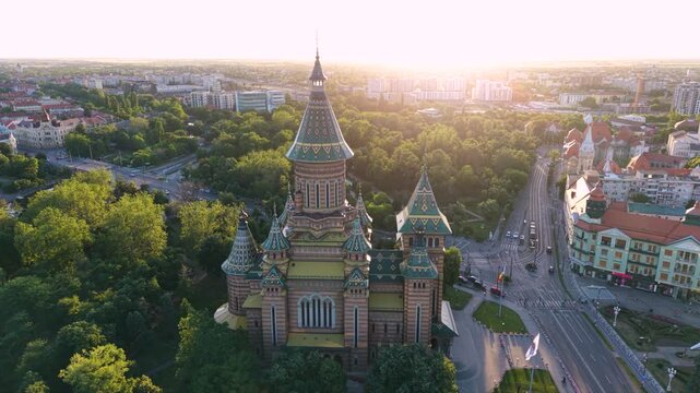 Aerial view of the Romanian Orthodox Metropolitan Cathedral in Timișoara, Romania, surrounded by dense green parkland, city streets and historic buildings in warm golden-hour light.
