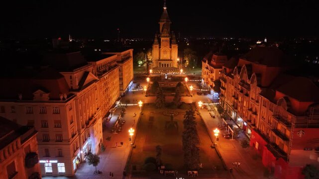 Night aerial view of the illuminated Romanian Orthodox Metropolitan Cathedral in Timișoara, Romania, surrounded by city streets, traffic and urban lights in the historic city centre.