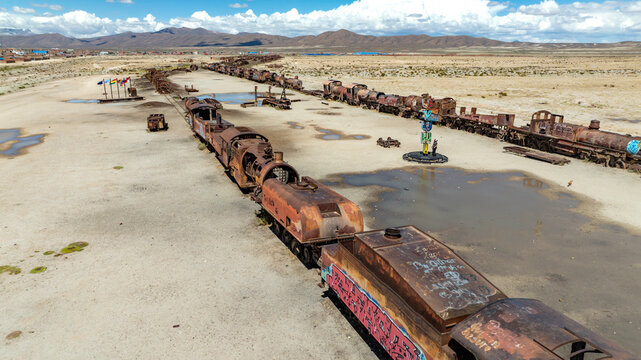 Train Cemetery featuring rusted locomotive skeletons and abandoned railway carriages scattered across the arid desert landscape. Aerial view.