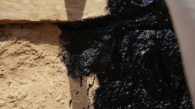 Black viscous bitumen slowly seeping from a natural rock formation, showcasing the natural geological process of crude oil migration and the sticky texture of fossil fuels