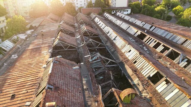 Aerial view of a severely damaged and partially collapsed industrial building roof, showing broken structural frames, deteriorated tiles and metal roofing on an abandoned factory complex.