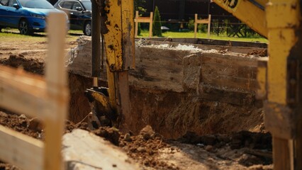 Fototapeta premium Excavator machine working on an earthwork project, digging a deep trench for new building foundation on a sunny day at a residential construction site