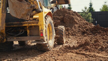 Fototapeta premium Yellow construction machinery performing earthworks, moving large piles of dirt and soil, creating tire tracks on the ground during a sunny day