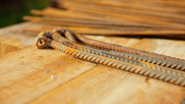 Rusty steel rebar rods lying on wooden planks, showing corrosion and detailed texture, ready for construction or building projects
