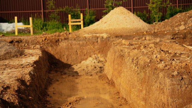 Construction site with an excavated trench and a pile of sand, preparing for a building's foundation, illustrating the initial stages of home development and project planning