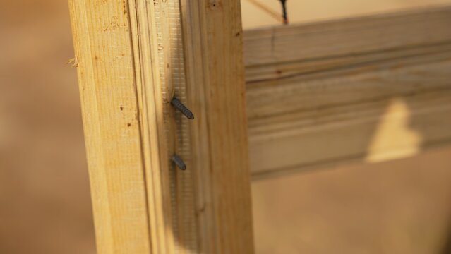 Wooden beam featuring two partially driven screws, illustrating the process of connecting parts for furniture assembly or repair, emphasizing craftsmanship and diy projects