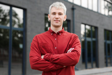 Obraz premium Portrait of smiling man in shirt with crossed arms in front of building outdoors