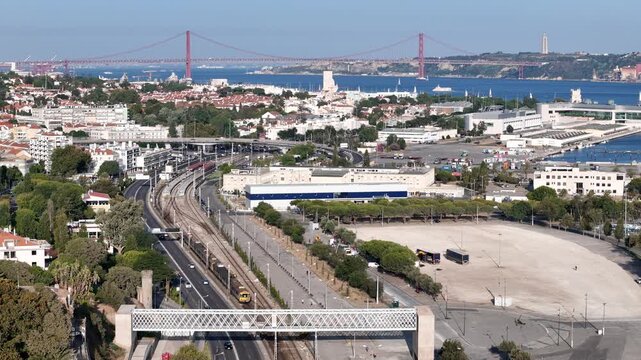 Aerial view of the 25 de Abril Bridge spanning the Tagus River with urban infrastructure, railway tracks, and the cityscape of Lisbon, Lisbon, Portugal.