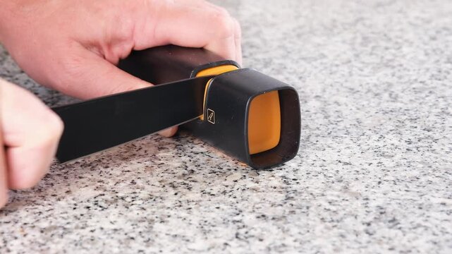 Close-up of sharpening a kitchen knife using a manual knife sharpener. Proper blade maintenance for cooking, food preparation, safety, precision and durability
