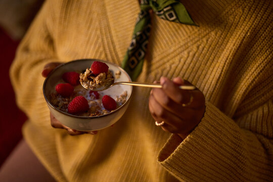 Cropped shot of Black woman holding bowl of granola with fresh raspberries and milk, eating healthy breakfast. Image represents morning routine, wellness, and organic nutrition marketing