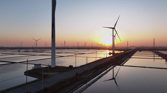 Wind farm at sunset with reflective water fields and orderly turbine arrays
