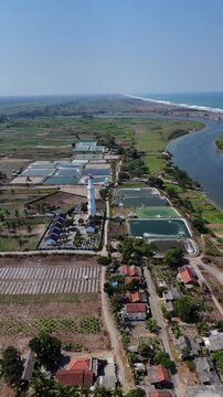 Aerial view of Tanggulangin Lighthouse surrounded by aquaculture ponds, agricultural fields, and rural houses in Kecamatan Kebumen, Jawa Tengah, Indonesia.