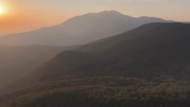 Aerial view of Cerreto Laghi mountains during golden hour with forest-covered slopes and soft sunset light, Cerreto Laghi, Emilia-Romagna, Italy.