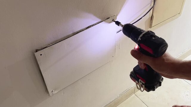 View from above of a construction worker's hands using a cordless power screwdriver to fix a drywall panel to a wall