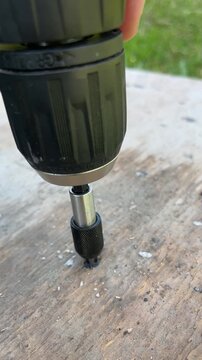 Close up view of a professional worker's hand using a cordless electric screwdriver to drive a screw into a wooden board