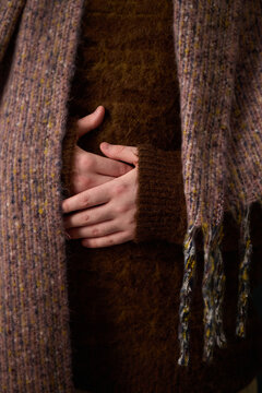 Close up of unrecognizable person in cozy sweater and headscarf holding hands on stomach, vertical
