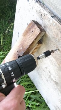 Carpenter's hand screwing a screw into wood with a cordless screwdriver for a renovation project showing the concept of construction, repair and manual work outdoors