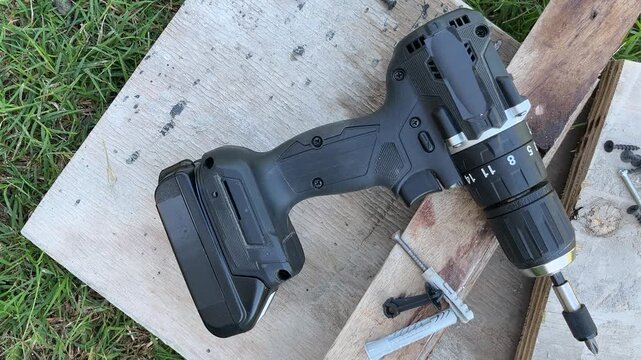 Top view of a cordless electric drill on a wooden board next to other construction items representing a home renovation project.