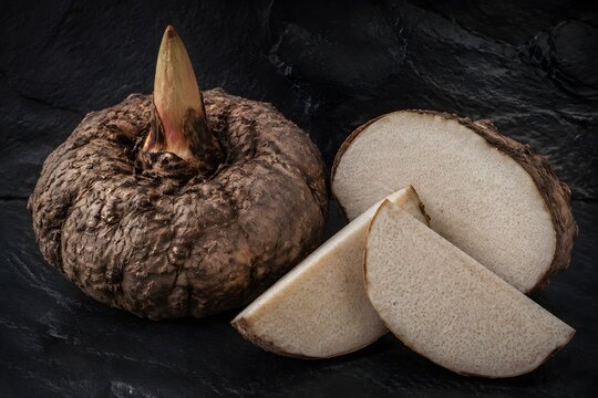 Fresh Konjac Corm Displayed Whole and Sliced Reveals Pale Speckled Flesh Against Charcoal Stone Photography