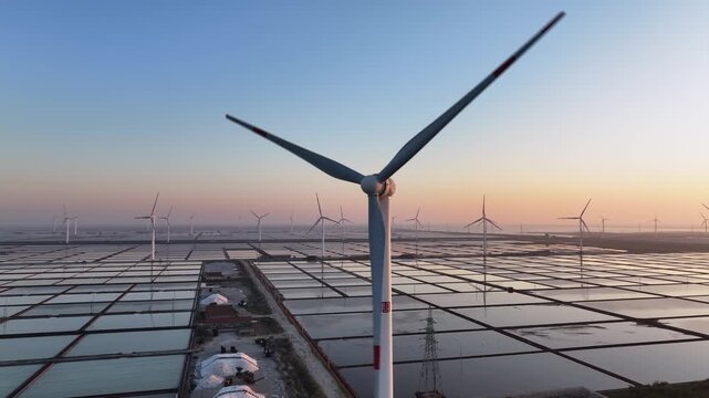 Wind farm at sunset over salt pans with reflective water surfaces and clear sky