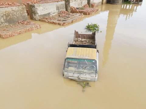 Aerial view of a truck partially submerged in floodwater near brick structures in Chhagalnaiya, Chittagong Division, Bangladesh.