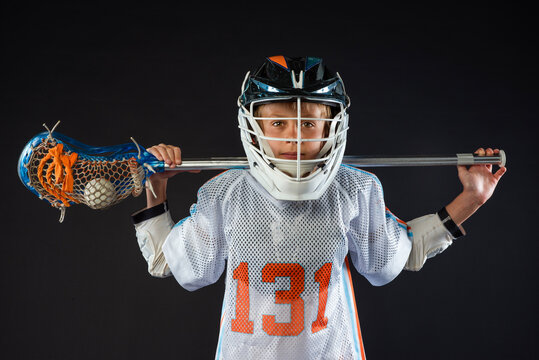 Youth lacrosse player in helmet holding stick across shoulders isolated on black background