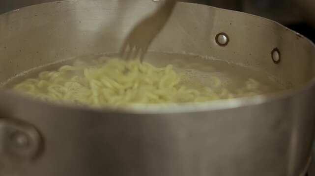 Someone stirring instant noodles. Steaming food. Close-up: instant ramen cooking in a pot on the stove. Pasta boiling in a pot. Steam rising from a pot. A pan of spaghetti over the stove. Zoom out