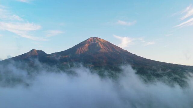 Aerial view of Mount Sindoro rising above clouds at sunrise near the Tambi tea garden in Wonosobo, Central Java, Indonesia.