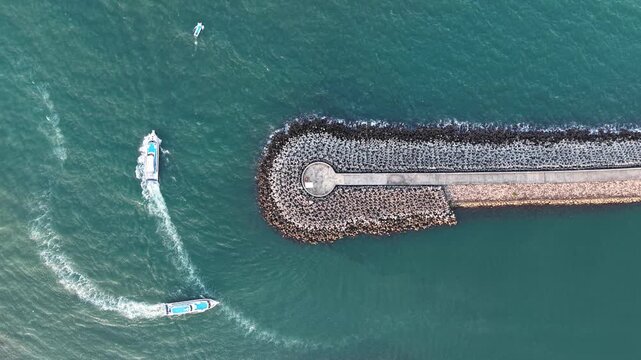 Aerial view of Sanur Harbour with boats navigating near the breakwater in the turquoise sea in Kecamatan Denpasar Selatan, Bali, Indonesia.